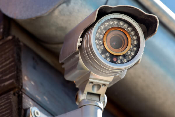 outdoor-bullet-security-camera-infrared-night-vision-metal-roof-eave-img Outdoor bullet security camera with infrared night vision mounted under a metal roof eave against a clear blue sky